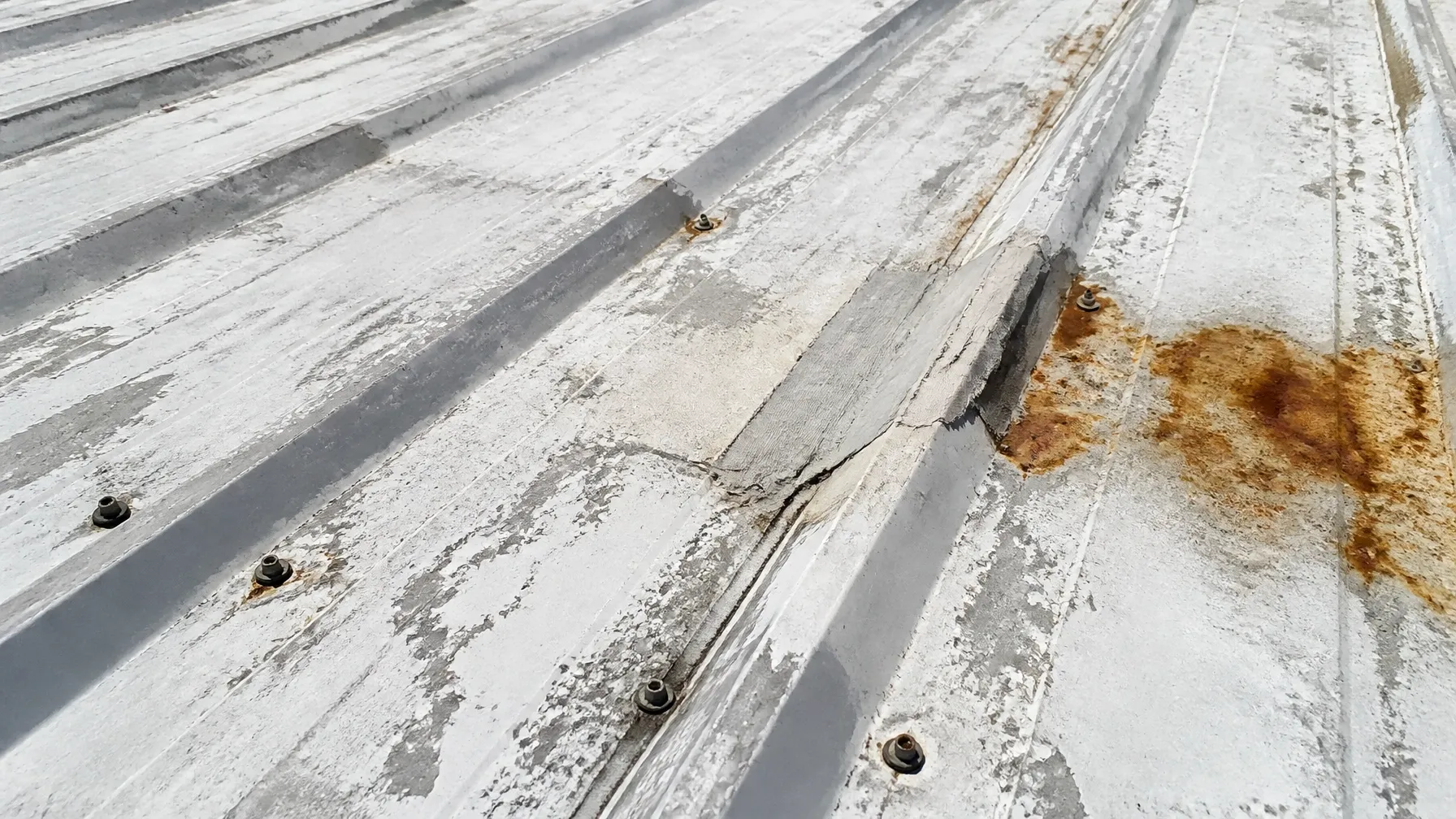Close-up of an aging self-storage metal roof with worn coating, seams, fasteners and rust